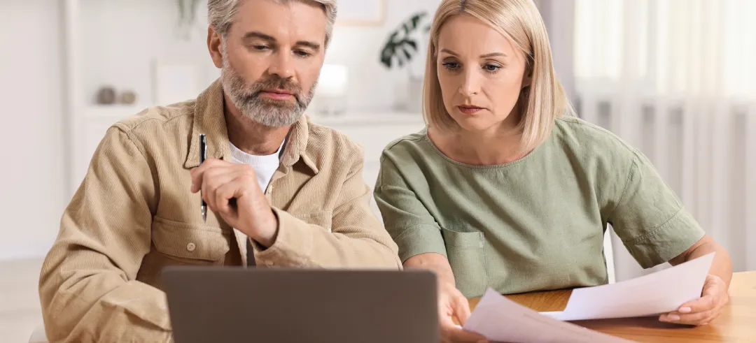 Pareja adulta comparando documentos físicos y en el ordenador